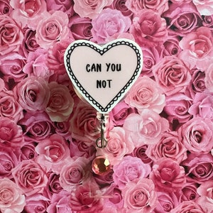 May include: A pink heart-shaped badge holder with the text "Can You Not" in black lettering. The badge holder is attached to a retractable badge reel with a pink rhinestone.