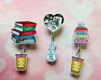 May include: Three colorful book stack themed retractable badge reels with a coffee and book theme. The first reel features a stack of books with the titles "A Court of Thorns and Roses", "A Court of Mist and Fury", "A Court of Wings and Ruin", "A Court of Silver Flames". The second reel features a black and white illustration of a skeleton reading a book with the text "I would love to buy my cat and I already made plans". The third reel features a stack of books with the titles "The Boy in the Striped Pajamas", "Adelle in Chains", "Six of Crows", "The Cruel Prince", "Throne of Glass" and a coffee cup with the text "All I need is iced coffee and books".