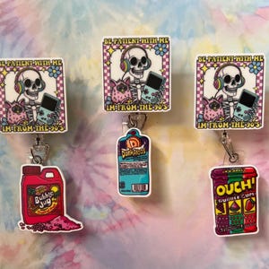 May include: Three retractable badge reels with colorful designs. The top design features a skeleton wearing headphones and holding a handheld game, with the text "BE PATIENT WITH ME" and "I'M FROM THE 90'S". Other designs include a Bubble Jug, Dunkaroos, and Ouch Bubble Gum.
