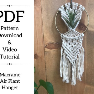 May include: A white macrame air plant hanger with a gold metal ring. The hanger is hanging on a wooden wall. The text "PDF Pattern Download & Video Tutorial Macrame Air Plant Hanger" is printed on a white background.