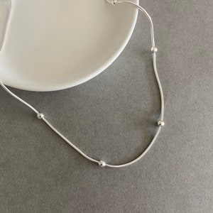 May include: A silver chain necklace with five small round beads.