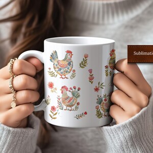 May include: White ceramic mug with a sublimation print of colorful chickens and floral designs. The mug is being held by a person's hands.