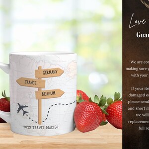 May include: White ceramic mug with a travel-themed design. The mug features a map with a dotted line and three wooden signs pointing to "France", "Germany", and "Belgium". The mug also has a small airplane graphic and the text "2025 Travel Diaries".