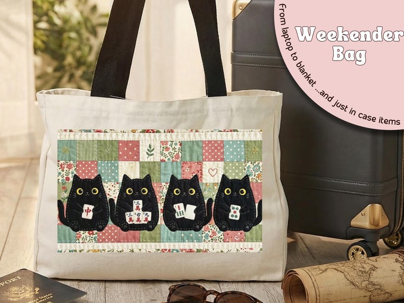 May include: A cream-colored canvas tote bag with black shoulder straps. The front features a rectangular patch with a patchwork quilt pattern in muted colors, displaying four black cats holding mahjong tiles with yellow eyes.