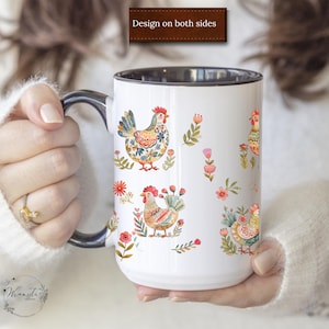 May include: White ceramic mug with a black rim and handle. The mug features a colorful design of chickens and flowers. The text "Design on both sides" is printed on the top of the mug.