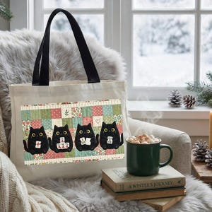 May include: A cream-colored canvas tote bag with black handles featuring a rectangular graphic of four black cats sitting in a row against a colorful patchwork quilt background, with each cat holding a small white mahjong tile in its paws.