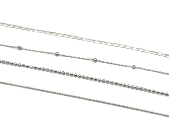 May include: Four silver chains of different styles and lengths. The chains are arranged in a layered fashion, with the longest chain at the top and the shortest chain at the bottom.