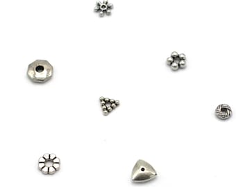 May include: Assortment of silver metal beads in various shapes, including a circle, a hexagon, a triangle, and a star. The beads have a hole in the center for stringing.