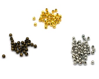 May include: Three piles of round metal beads in different colors: gold, bronze, and silver. The beads are small and uniform in size.