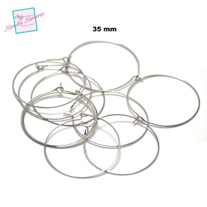 Pu&ograve; includere: Un set di sei orecchini a cerchio argentati, ognuno con un diametro di 35 mm. Gli orecchini sono disposti in una pila, con alcuni che si sovrappongono.