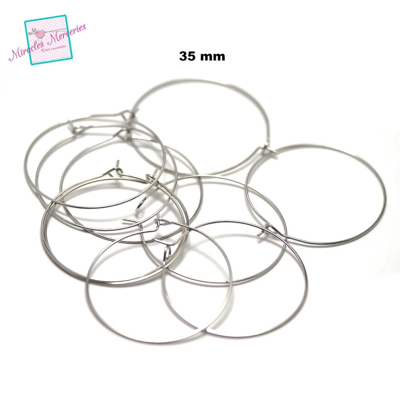 Pu&ograve; includere: Un set di sei orecchini a cerchio argentati, ognuno con un diametro di 35 mm. Gli orecchini sono disposti in una pila, con alcuni che si sovrappongono.