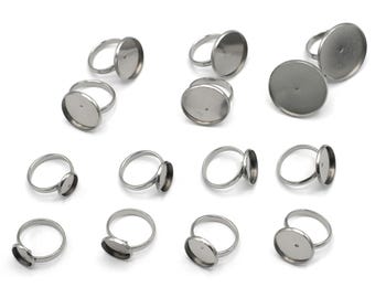 May include: A set of 12 silver-toned ring blanks with round bezels. The bezels are designed to hold a cabochon or other flat-backed embellishment.