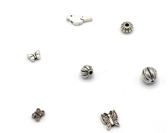 May include: A collection of small, silver-colored beads and charms. The assortment includes butterfly, bird, and flower shapes, along with various round and textured beads. The items are scattered on a white surface, offering a variety of options for jewelry making and crafting.