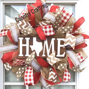 May include: A red, white, and brown wreath with a wooden sign that says "HOME" with the state of Texas in the middle of the word. The wreath is decorated with burlap, checkered ribbon, and white lace.