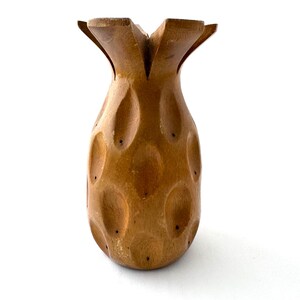 May include: A wooden pineapple shaped utensil holder. The holder is carved with a textured surface and has a brown color.