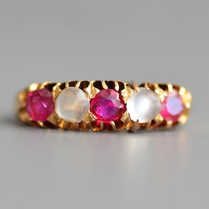 May include: A gold band ring with alternating red rubies and white moonstones.
