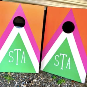 May include: Two wooden game boards with a pink, white, and green geometric design. The boards have the word "STA" written on them.
