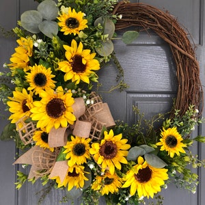 May include: A sunflower wreath with burlap ribbon and greenery. The wreath is made of grapevine and features a variety of sunflowers in different sizes. The wreath is perfect for adding a touch of summer to your home decor.