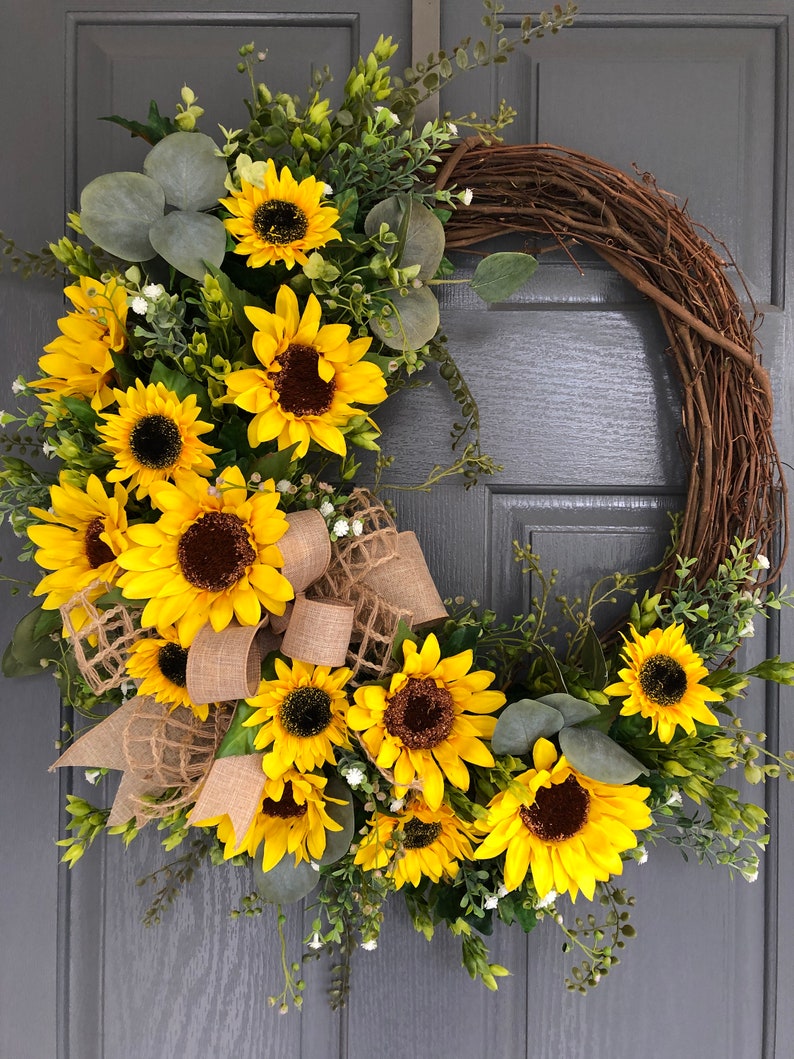 May include: A sunflower wreath with burlap ribbon and greenery. The wreath is made of grapevine and features a variety of sunflowers in different sizes. The wreath is perfect for adding a touch of summer to your home decor.