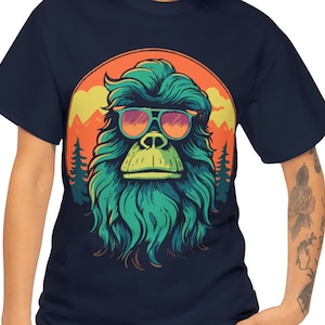 May include: A navy blue t-shirt with a graphic of a green, furry creature wearing sunglasses. The creature has a mountain range and a sunset behind it.