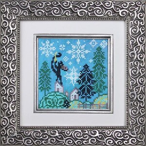 May include: Cross-stitch artwork of a winter scene, framed in a silver-colored, ornate frame. The artwork depicts a black figure with a staff, snowflakes, evergreen trees, and small buildings against a blue sky. The frame has a detailed, swirling pattern.