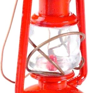 May include: A miniature red lantern featuring a bright red metal frame, a clear glass globe, and a thin wire handle. The lantern has a cylindrical base, a central glass section protected by a wire cage, and a tiered top cap with a small loop.