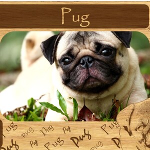 May include: A wooden picture frame with a brown background and a cutout of a pug dog. The frame has the word "Pug" written in brown text at the top and the word "Pug" written multiple times in a smaller font around the border.