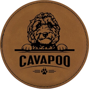 May include: A brown leather coaster with a black silhouette of a Cavapoo dog peeking over the top. The text "CAVAPOO" is printed below the dog, with a paw print symbol underneath.