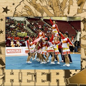 May include: A group of cheerleaders in red and white uniforms perform a stunt in a gymnasium. The cheerleaders are smiling and appear to be having fun. The background shows a crowd of people watching the performance.