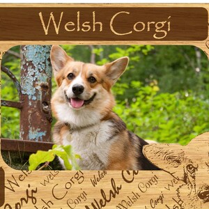 May include: Wooden picture frame featuring a smiling Welsh Corgi dog. The frame has a brown finish with the words "Welsh Corgi" engraved on the top and sides. Paw prints and a dog bone are also featured.