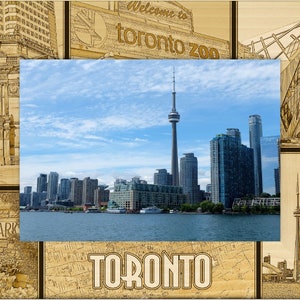 May include: A wooden framed image featuring the Toronto skyline with the CN Tower, surrounded by architectural sketches and the words "Welcome to Toronto Zoo", "High Park", and "Toronto". The central image shows a blue sky and water.