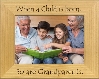May include: A wooden picture frame with the text "When a child is born... So are Grandparents."  The frame contains a photo of a family reading a book together.