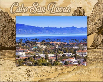 May include: A framed photograph of a coastal town with the words "Cabo San Lucas" printed at the top. The photo shows a view of the town from a hilltop, with the ocean and mountains in the background.