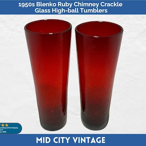 May include: Two vintage ruby red Blenko glass high-ball tumblers. The glasses have a chimney crackle design and a tall, slender shape. The text "1950s Blenko Ruby Chimney Crackle Glass High-ball Tumblers" is at the top.