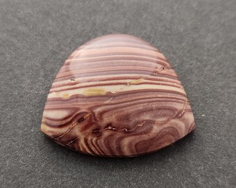 Op de afbeelding: Een driehoekige cabochon van gebande agaat met bruine, witte en roze strepen. De steen is gepolijst en heeft een gladde, glanzende afwerking.