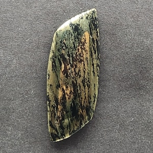 Pode incluir: Uma gema cabochão verde, preta e dourada com um padrão único e em espiral. A gema é cortada em forma de lágrima e tem uma superfície lisa e polida.