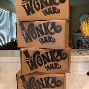 May include: Four brown cardboard boxes stacked on top of each other. Each box has a black and white graphic of a top hat and the words "Wonka Bar" printed on the front.