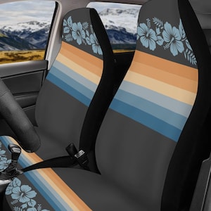 May include: A pair of car seat covers featuring a dark gray base with a horizontal pattern of light blue, beige, and orange stripes. The design includes light blue hibiscus flower and leaf illustrations positioned at the top and bottom sections.