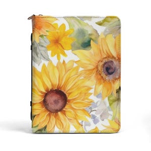 May include: A zippered journal with a watercolour design of yellow sunflowers with brown centres and green leaves on a white background. The floral pattern is repeated across the cover.