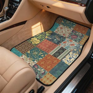 May include: A rectangular car floor mat featuring a patchwork design of various floral and botanical patterns in shades of teal, rust orange, cream, and dark green, with a small moth illustration integrated into one of the patterned squares.