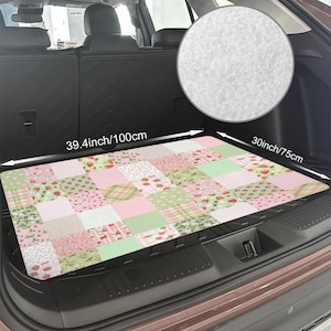 May include: A rectangular car trunk mat featuring a patchwork design of pink, green, and white squares with strawberry, floral, and gingham patterns. It measures 39.4 inches by 30 inches and has a textured, light gray felt-like underside.