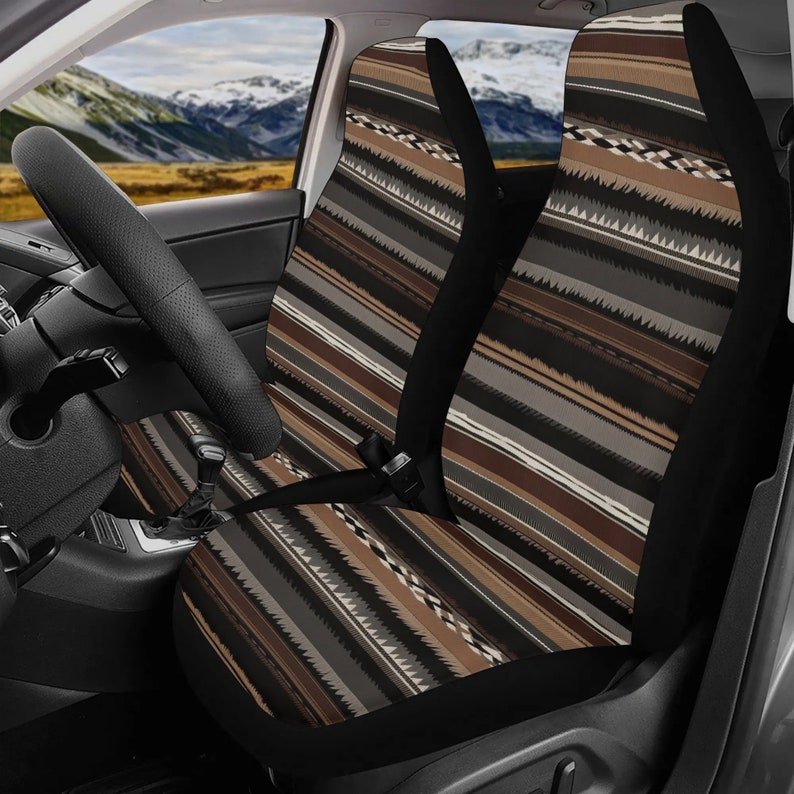 May include: Car seat covers with a geometric pattern in shades of brown, gray, and black. The design features vertical stripes and zigzag elements, creating a textured appearance. The covers are installed in a car, with the steering wheel visible.