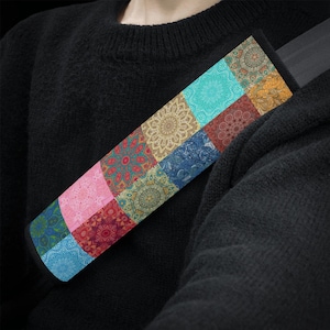May include: A rectangular seat belt cover featuring a vibrant patchwork design of various mandala patterns in shades of turquoise, pink, deep red, gold, blue, and green. The fabric accessory is wrapped around a black seat belt strap.
