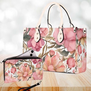 May include: A set of two floral patterned handbags. The larger bag has a cream-coloured handle and a zip closure. The smaller bag has a black zip and a wrist strap. Both bags feature a pink and white floral design.