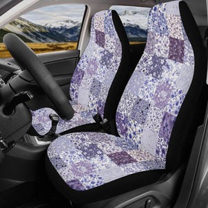 May include: A pair of car seat covers featuring a patchwork design of various floral patterns in shades of purple, lavender, and white. The covers are fitted over the front seats of a vehicle, displaying a repeating square grid of botanical prints.