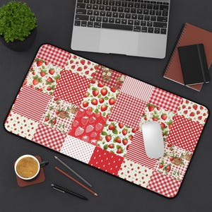 Może przedstawiać: Prostokątna podkładka pod biurko z patchworkowym wzorem z truskawkami, czerwoną kratą, kropkami i paskami. Mata ma czarną obwódkę, a na niej znajduje się biała mysz komputerowa.