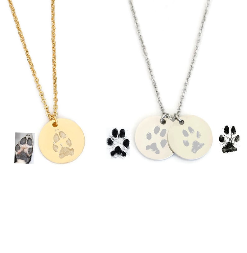 May include: Two necklaces with paw print pendants. One necklace has a gold pendant with a single paw print. The other necklace has two silver pendants with paw prints. The paw prints are black and white.