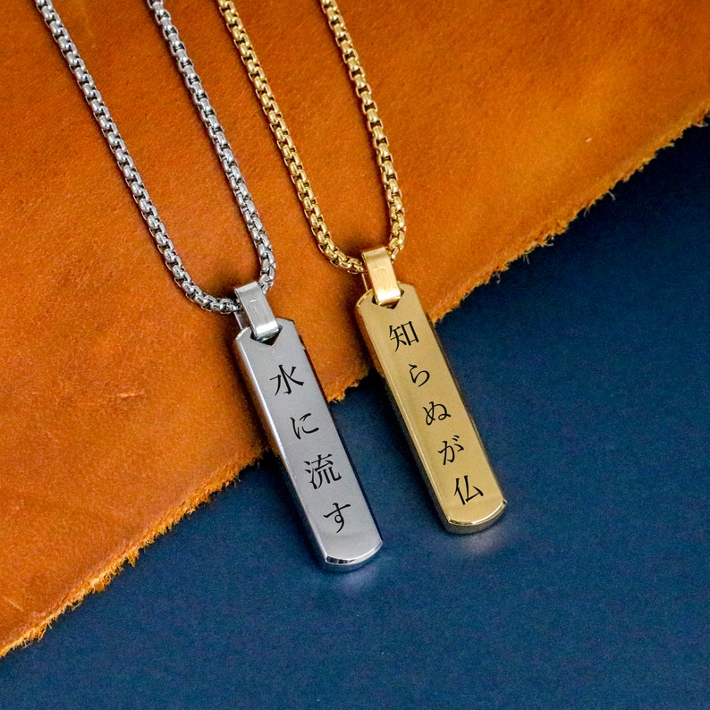 May include: Two silver and gold necklaces with engraved pendants. The silver pendant reads "水に流す" and the gold pendant reads "知らぬが化".