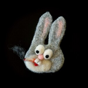 May include: A gray felt bunny head with large white eyes, pink inner ears, and a pink nose. The bunny is smoking a cigarette. The background is black.