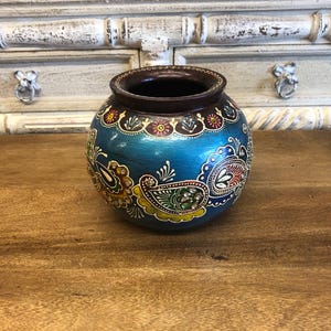 May include: A blue and brown ceramic pot with intricate floral and paisley designs painted in gold, red, and green.